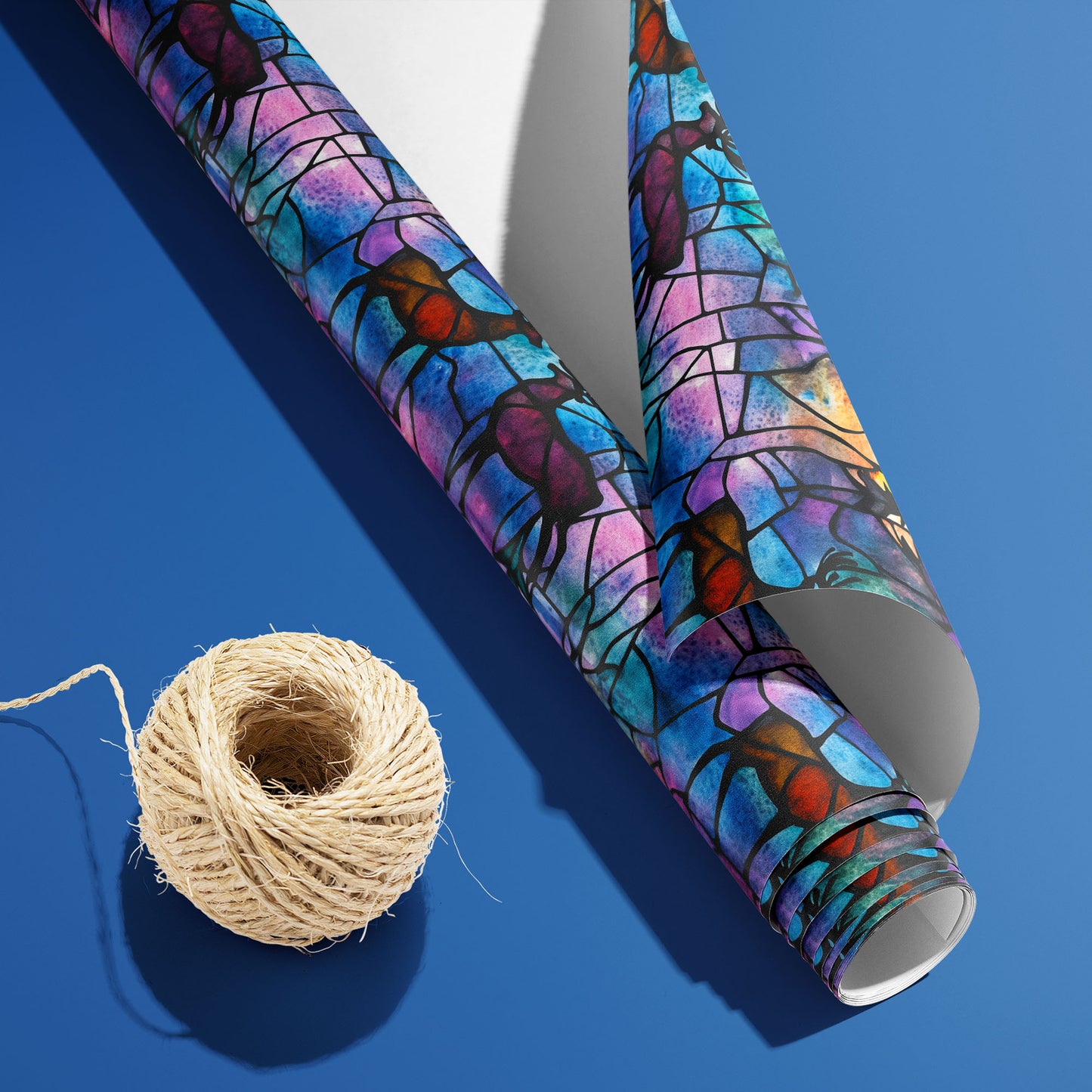 A partially unfurled Majestic Nightfall roll with the white underside visible beside a spool of natural twine, featuring jewel-tone deer and pines on a cobalt blue surface.
