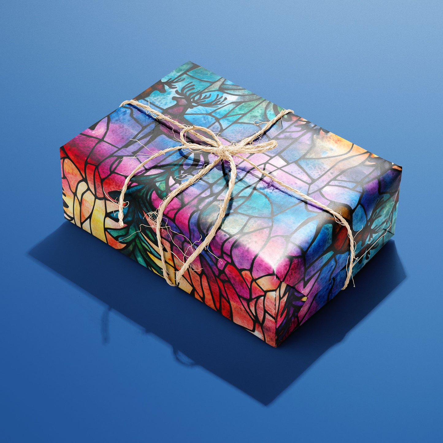 A single rectangular gift wrapped in Majestic Nightfall—stained-glass deer and pine boughs in vivid jewel tones—tied with natural twine on a cobalt blue background.