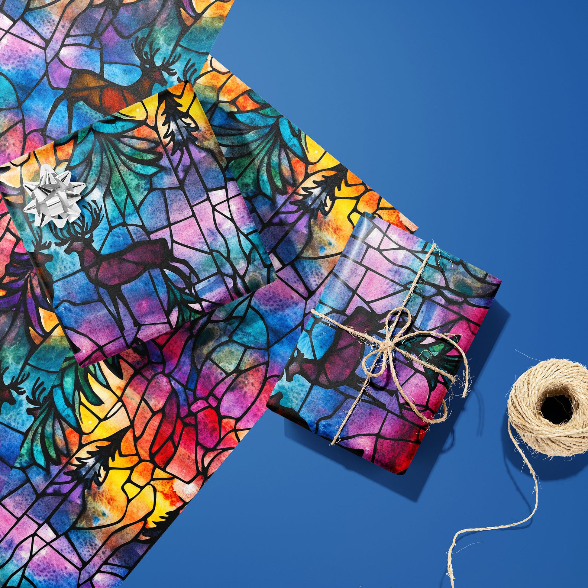 Two gifts in Majestic Nightfall wrap—one with a silver bow and one tied with twine—rest on two unused sheets beside a spool of twine on a cobalt blue background.
