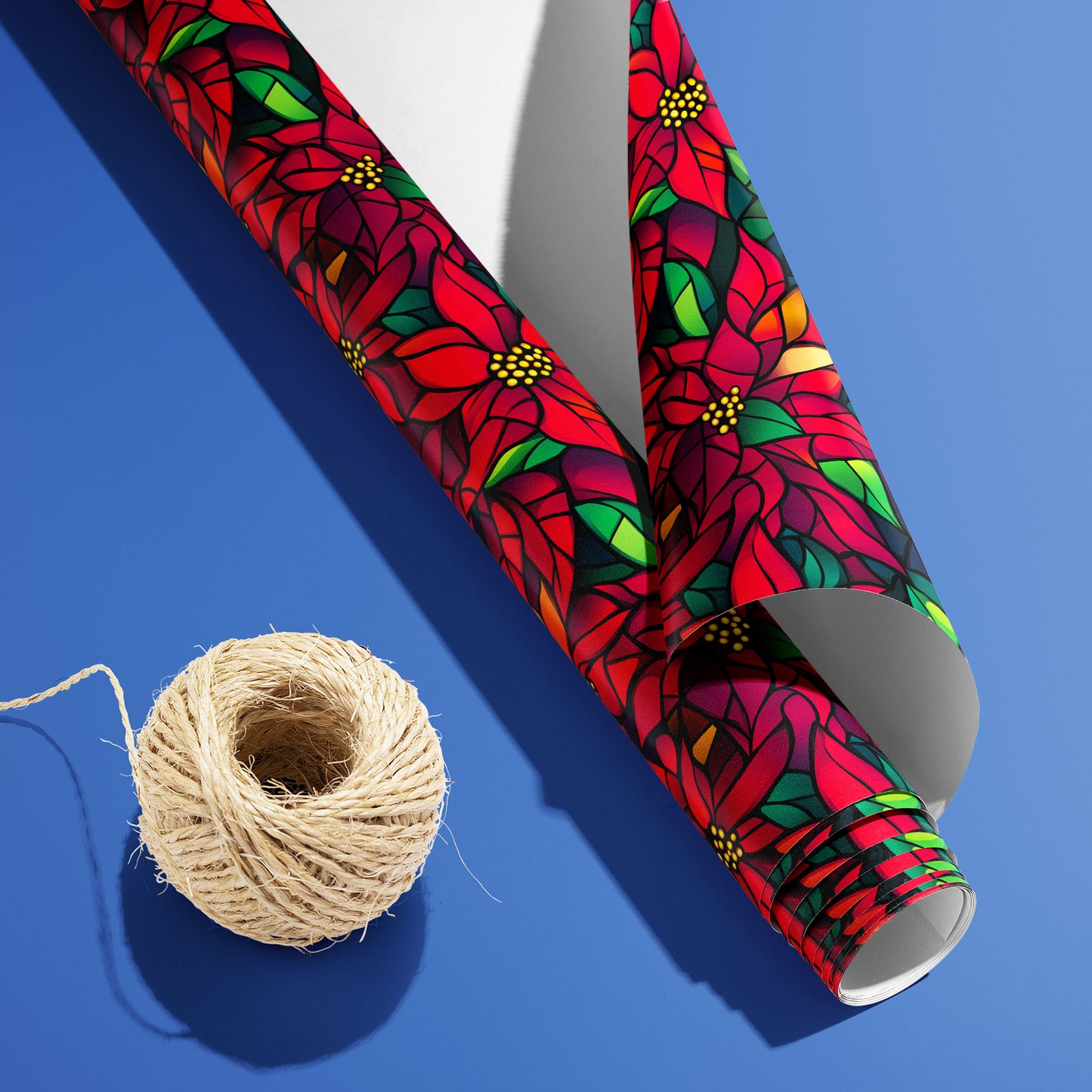 A partially unfurled roll of Poinsettia Prism with the white underside visible beside a spool of natural twine, showing stained-glass poinsettias on black over cobalt blue.