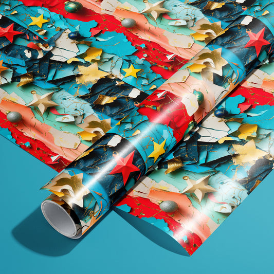 A roll of Starry Collage wrapping paper resting on a matching unrolled sheet, featuring layered collage textures with bright stars, ornaments, and gold flecks on a teal background.