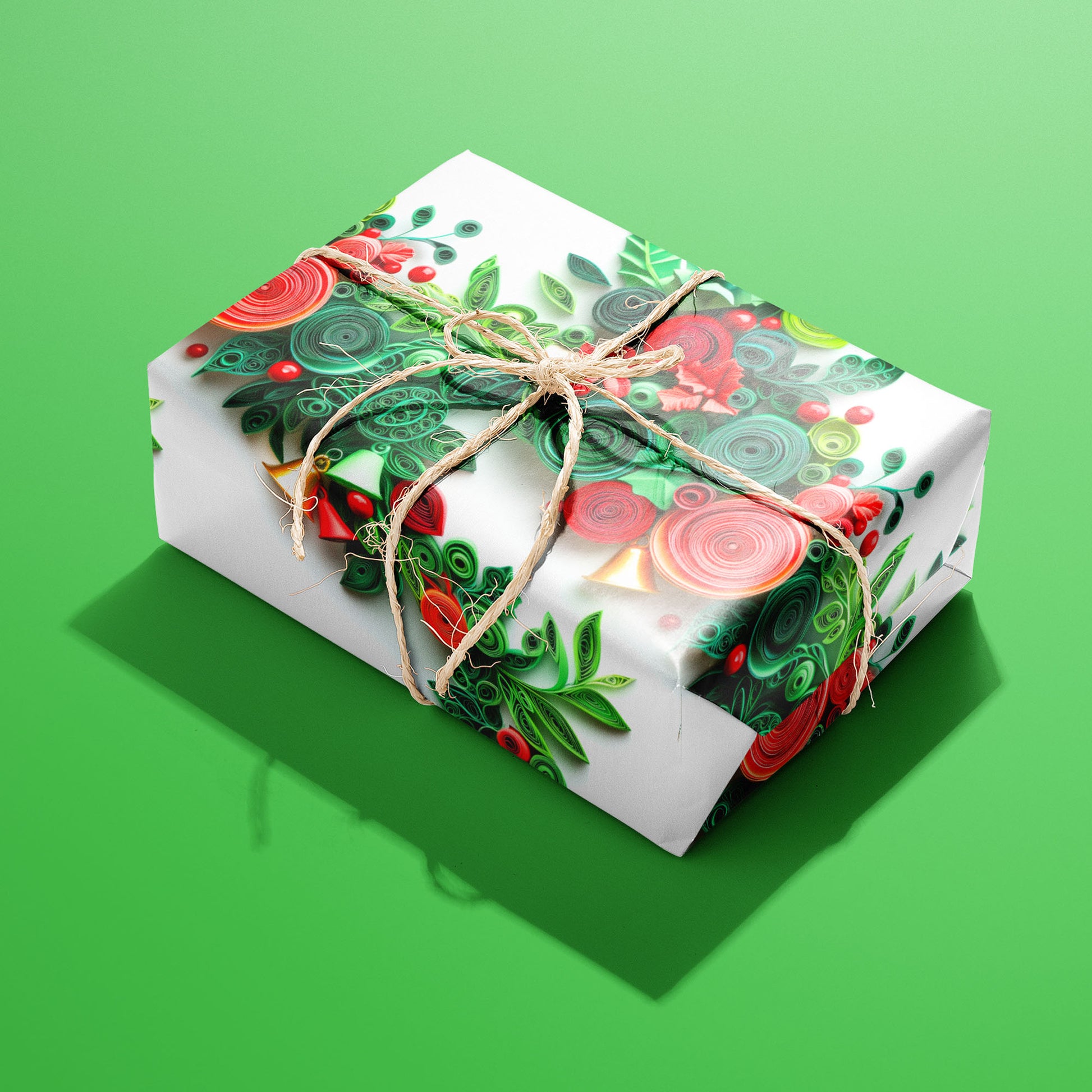 A single gift wrapped in Festive Quills and tied with natural twine, revealing quilled spirals with holly, poinsettias, and bells on white, set on a bright green surface.
