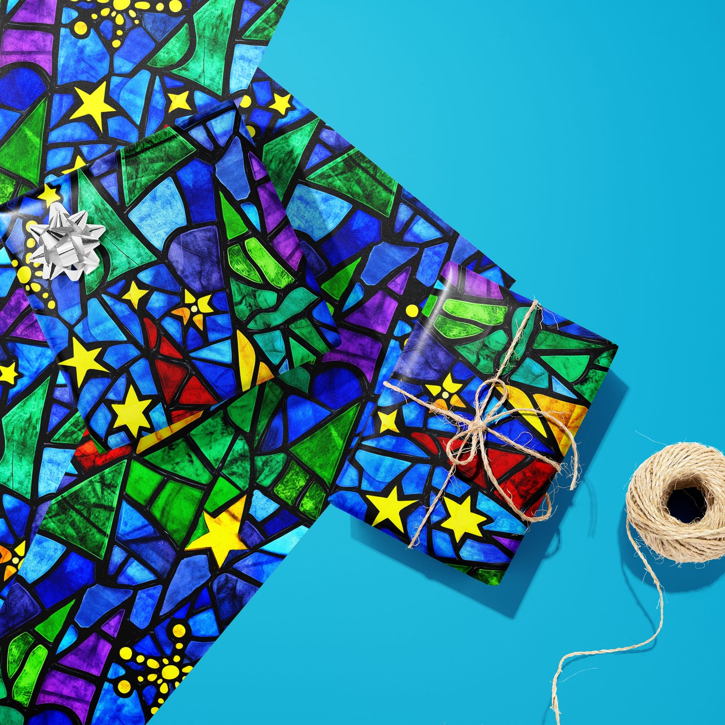 Two Starlit Holiday gifts—one with a silver bow and one tied with twine—rest on two unused sheets beside a twine spool on a bright cyan surface, showing stained-glass stars and trees.