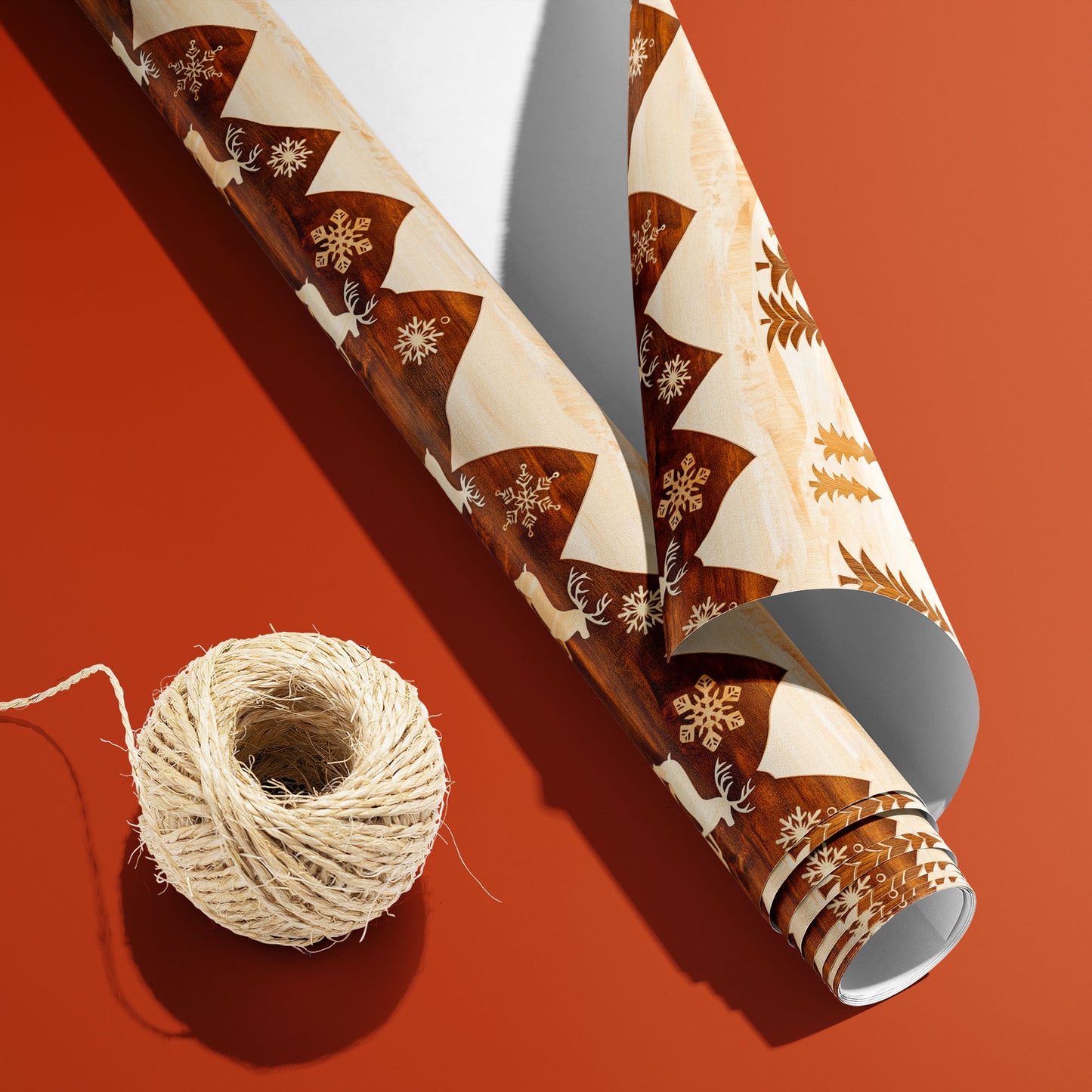 A partially unfurled roll of Rustic Reindeer with the white underside visible sits beside natural twine on burnt orange, revealing woodgrain reindeer and trees on cream.