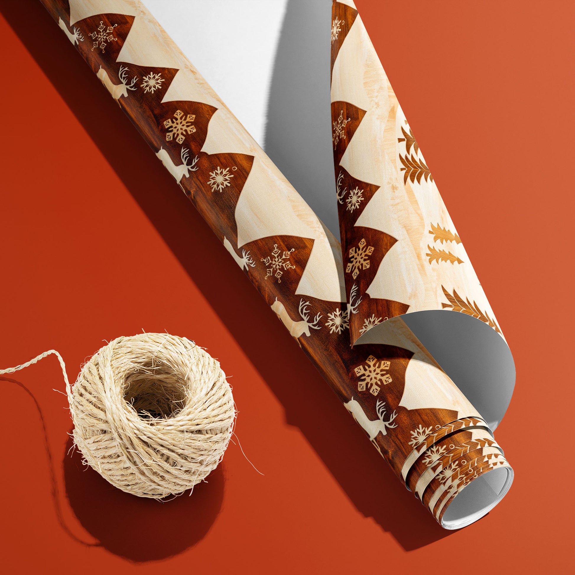 A partially unfurled roll of Rustic Reindeer with the white underside visible sits beside natural twine on burnt orange, revealing woodgrain reindeer and trees on cream.