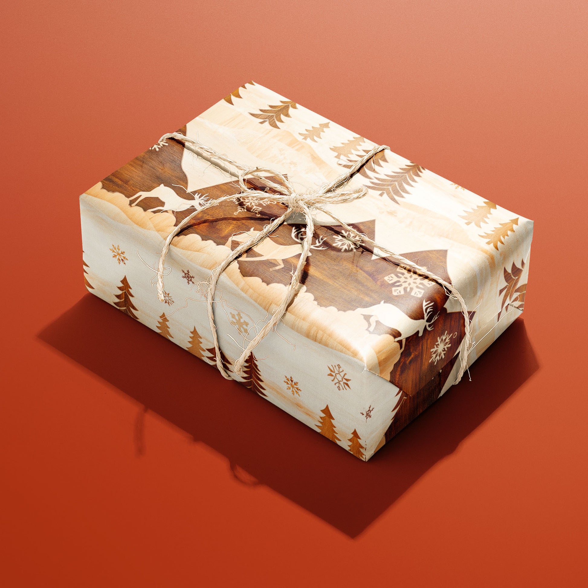 A single gift wrapped in Rustic Reindeer and tied with natural twine shows wood-inlay reindeer, fir trees, and snowflakes on a cream ground against a burnt-orange background.