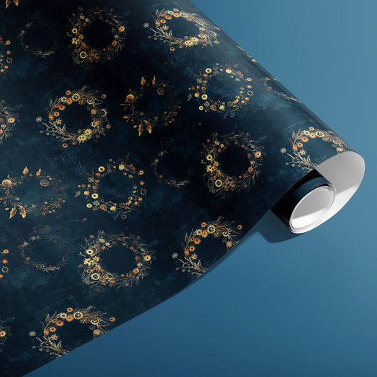 A partially unfurled roll of Gilded Gears paper reveals golden gear-and-holly wreaths on a deep navy ground against a cool blue backdrop.