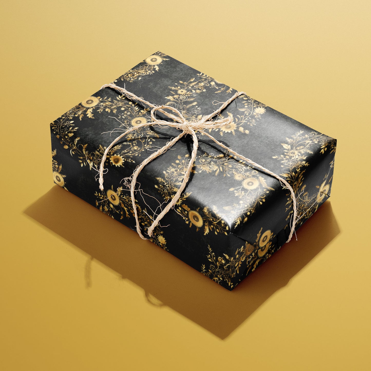A single rectangular gift wrapped in Clockwork Wreaths and tied with natural twine, displaying gold cog-and-vine wreaths against a charcoal-black background on mustard yellow.