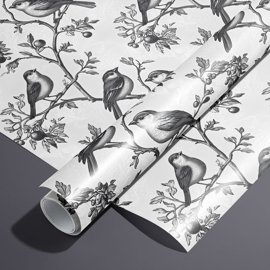 A roll of Winter Aviary rests on an unrolled sheet, showing engraved songbirds perched on berry-laden branches over a soft white damask ground, styled on a charcoal gray surface.