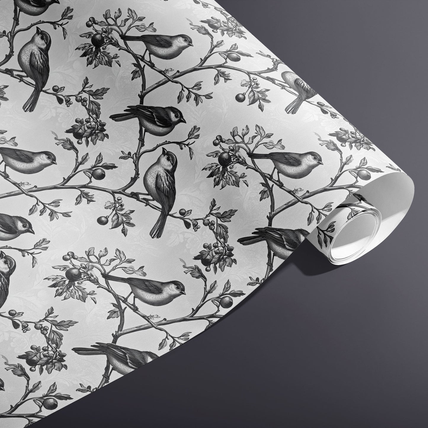 A partially unfurled roll of Winter Aviary gift wrap reveals monochrome birds and berries on a subtle damask white ground against a charcoal gray background.