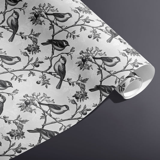 A partially unfurled roll of Winter Aviary gift wrap reveals monochrome birds and berries on a subtle damask white ground against a charcoal gray background.