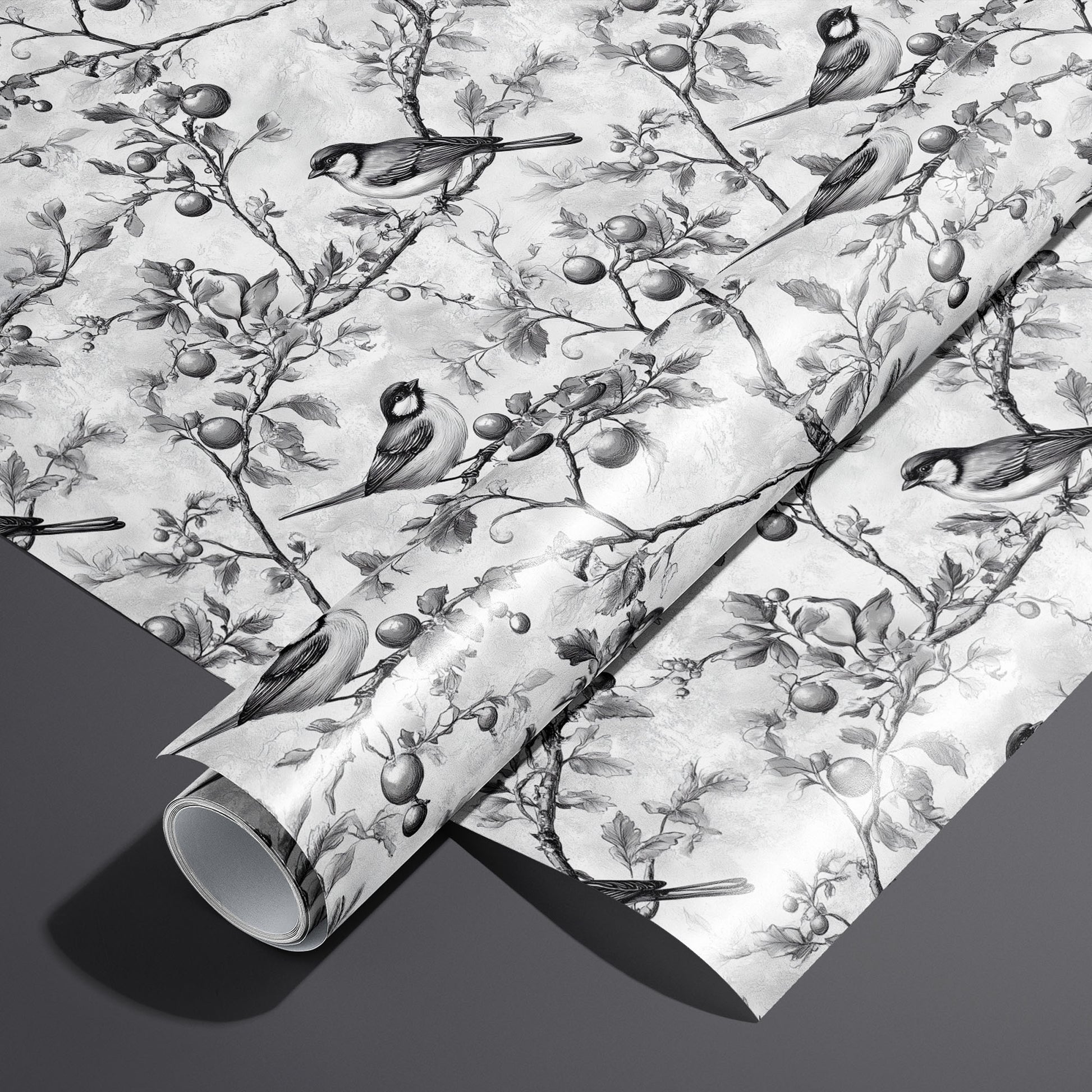 A roll on an unrolled sheet of Winter Orchard wrapping paper with etched songbirds on fruiting branches over a frosty gray ground, set on a dark charcoal background.
