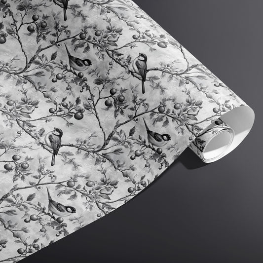 A partially unfurled roll of Winter Orchard wrapping paper showing monochrome birds and orchard branches on a misty gray ground against a dark charcoal background.