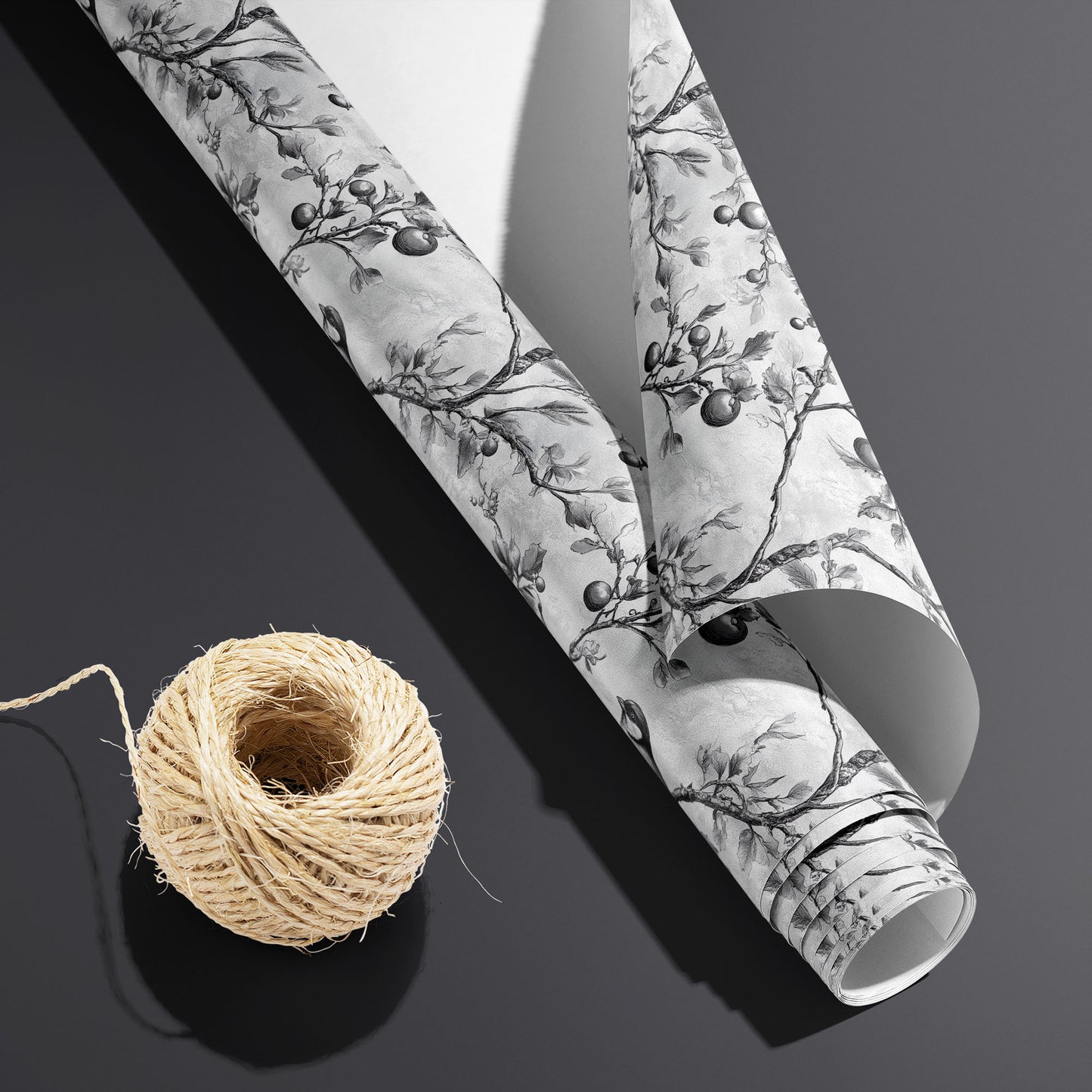 A partially unfurled Winter Orchard roll with the white underside visible beside a spool of natural twine, featuring etched birds and fruiting branches on a dark charcoal background.