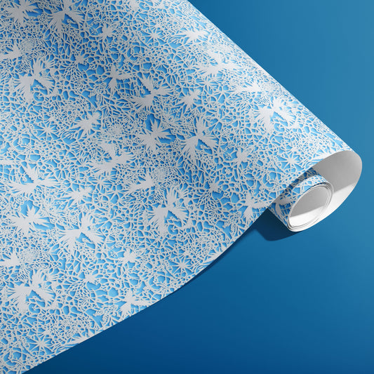 A partially unfurled roll of Winter's Whisper reveals delicate white botanical filigree and snowflakes on an icy blue field against a deep blue backdrop.
