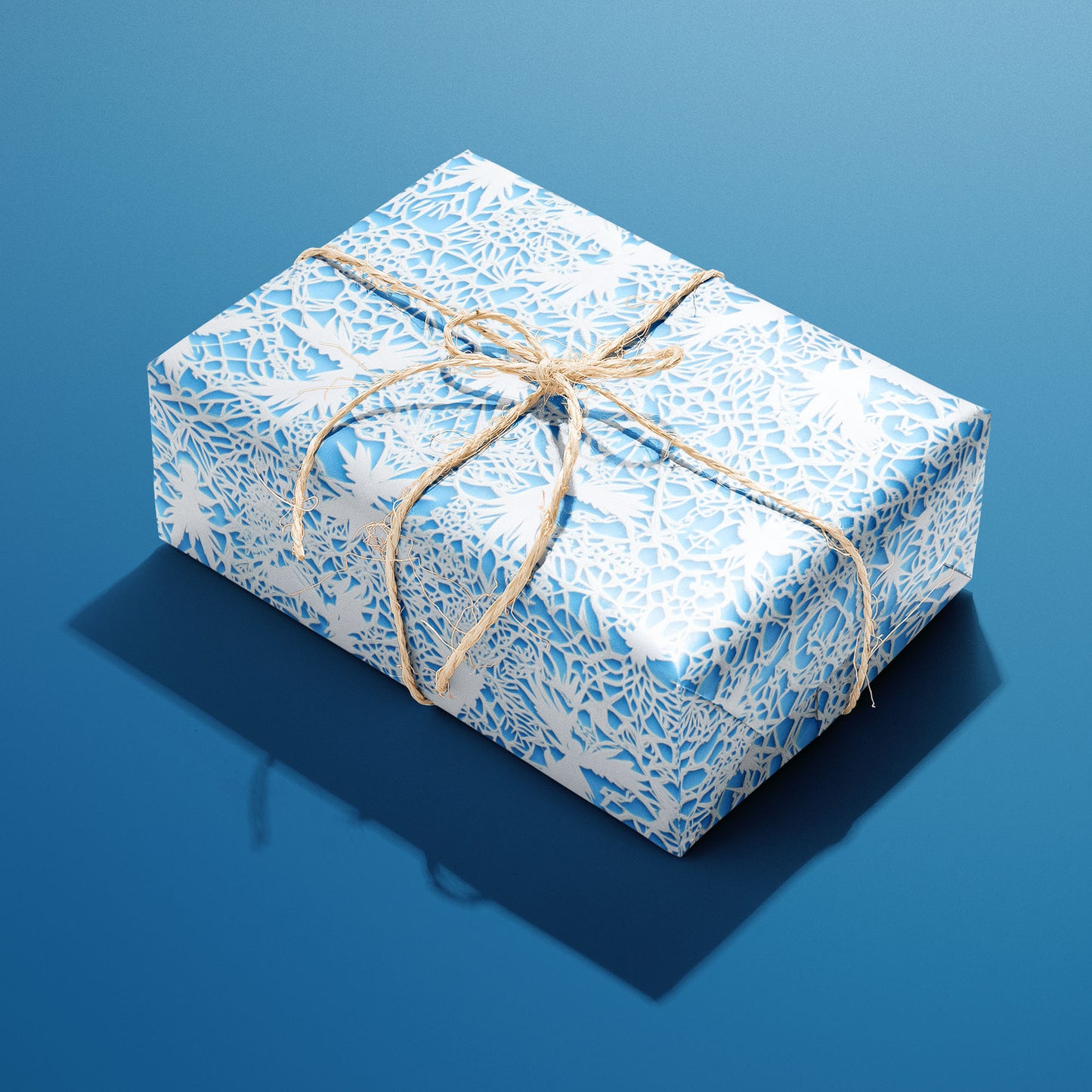 A single gift wrapped in Winter's Whisper and tied with natural twine shows white lace-cut winter florals and snowflakes on icy blue against a deep blue background.