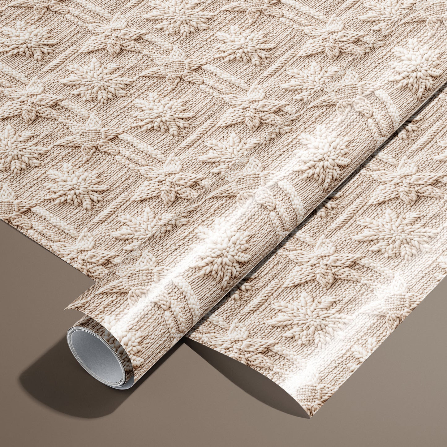 A roll of Winter Weave wrapping paper rests on an unrolled sheet, showing a cozy knit-style snowflake pattern in cream and beige on a warm brown surface.
