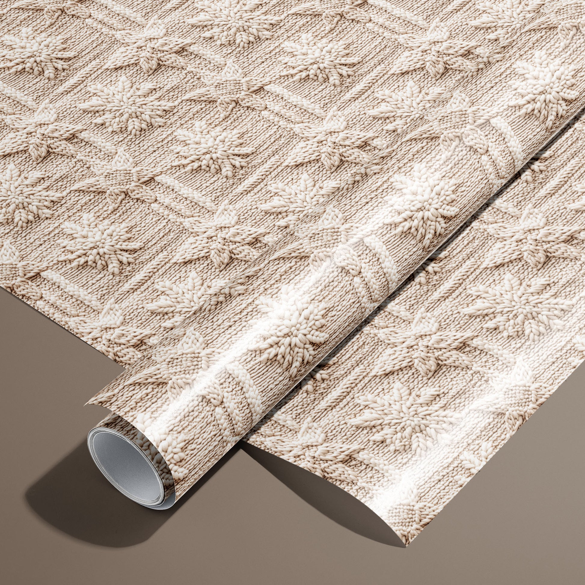 A roll of Winter Weave wrapping paper rests on an unrolled sheet, showing a cozy knit-style snowflake pattern in cream and beige on a warm brown surface.