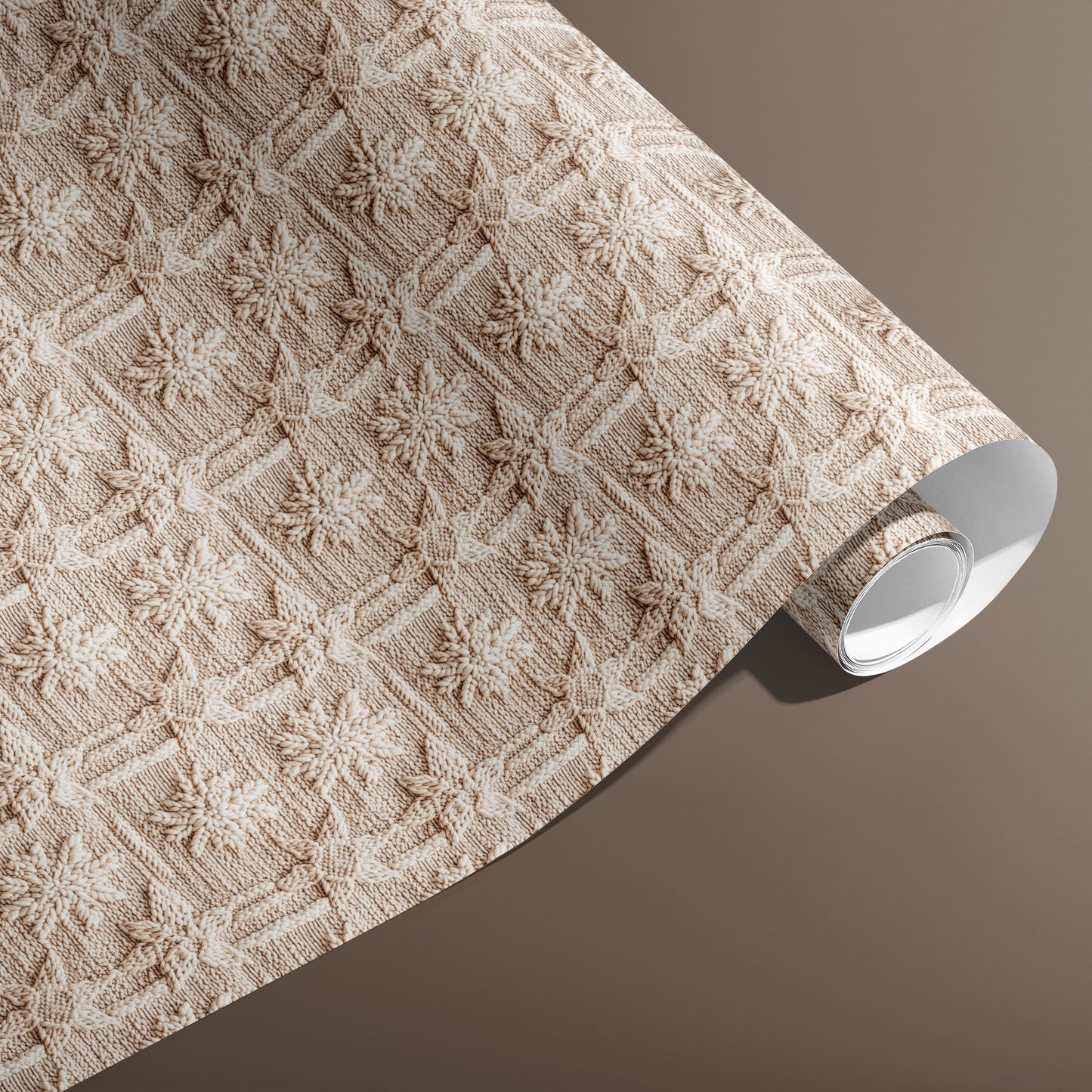A partially unfurled roll of Winter Weave gift wrap displays a textured knit snowflake motif in soft cream and beige against a warm brown background.