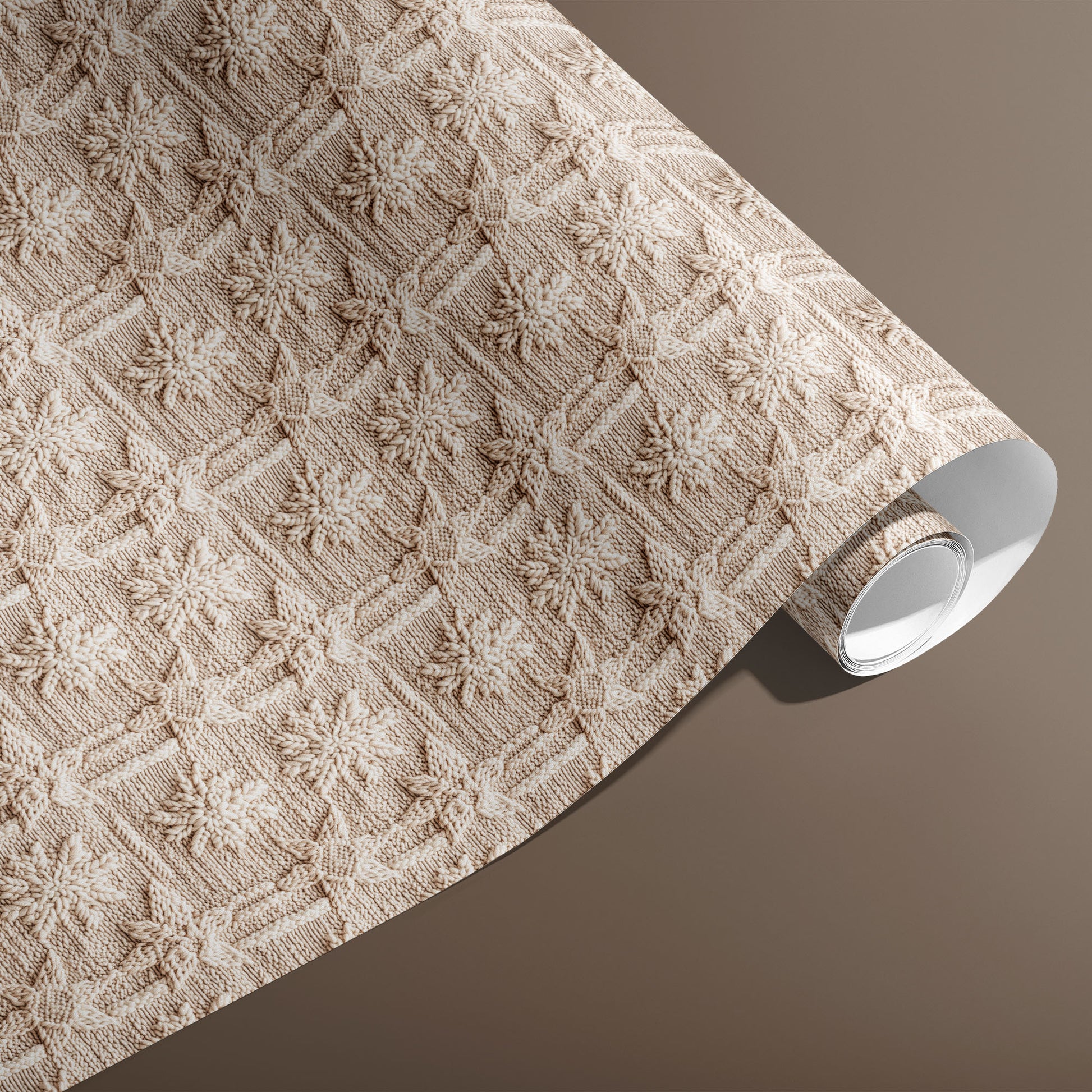 A partially unfurled roll of Winter Weave gift wrap displays a textured knit snowflake motif in soft cream and beige against a warm brown background.