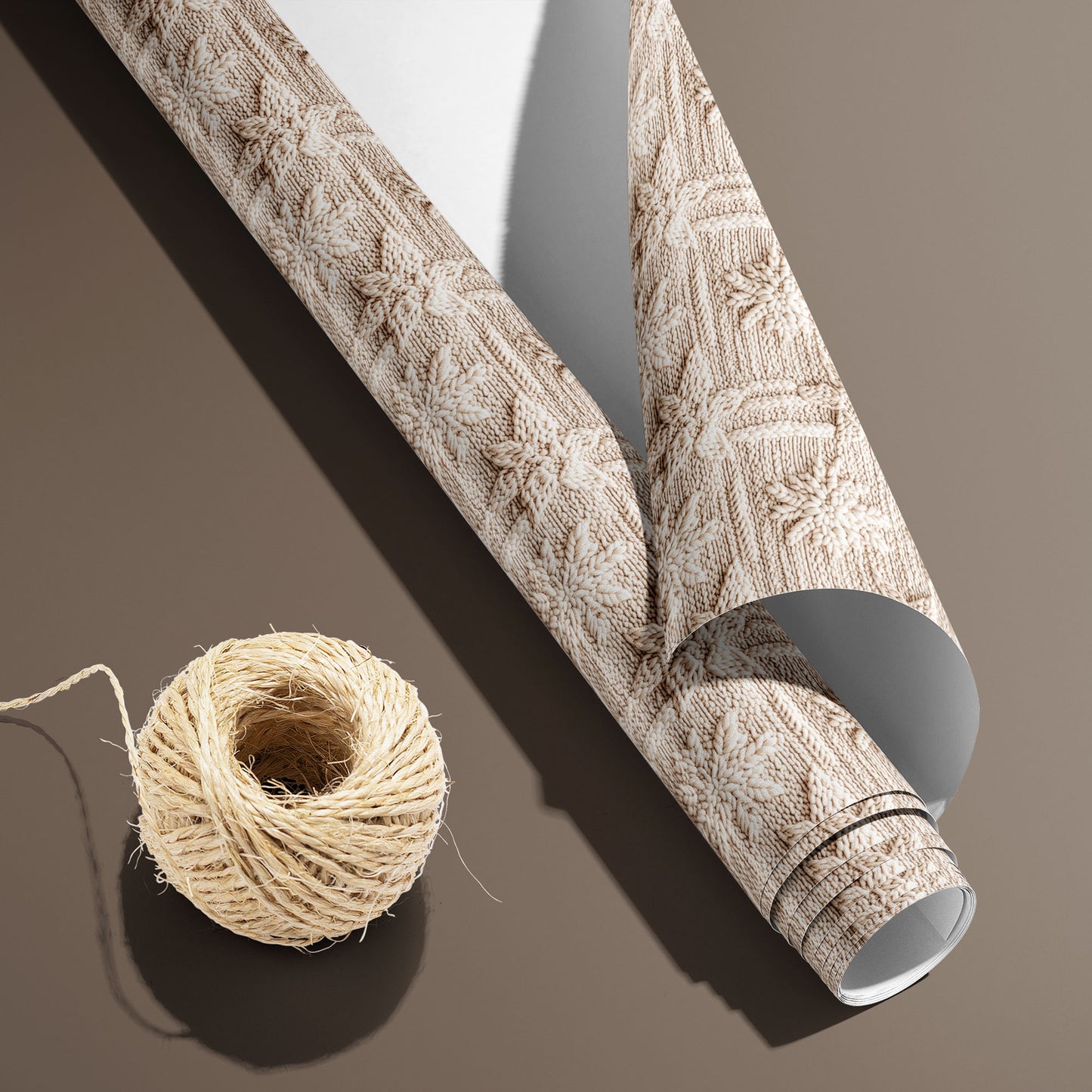 A partially unfurled roll of Winter Weave, white underside visible beside a spool of natural twine, shows a knit snowflake pattern on a warm brown surface.