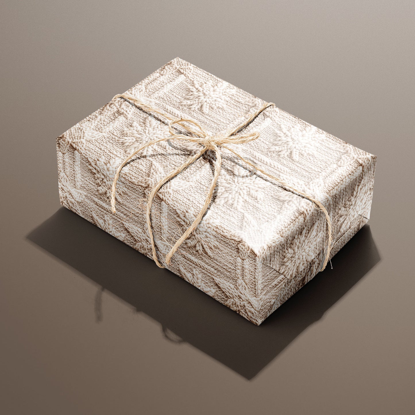 A single rectangular gift wrapped in Winter Weave and tied with natural twine highlights a cozy knit snowflake design in cream and beige on a warm brown backdrop.
