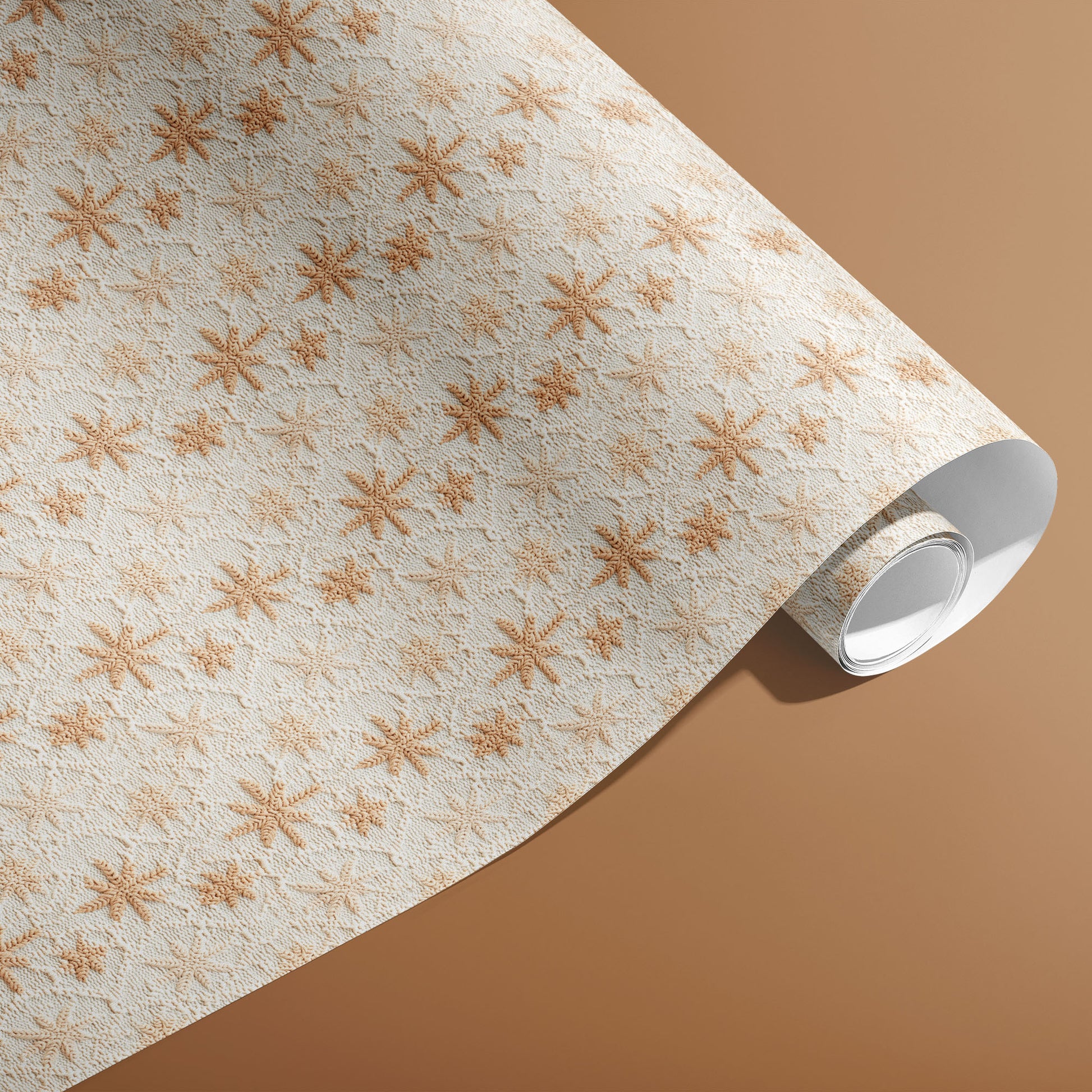 A partially unfurled roll of Hygge Holiday paper showing cozy knit snowflake motifs in tan on white against a caramel-brown backdrop.