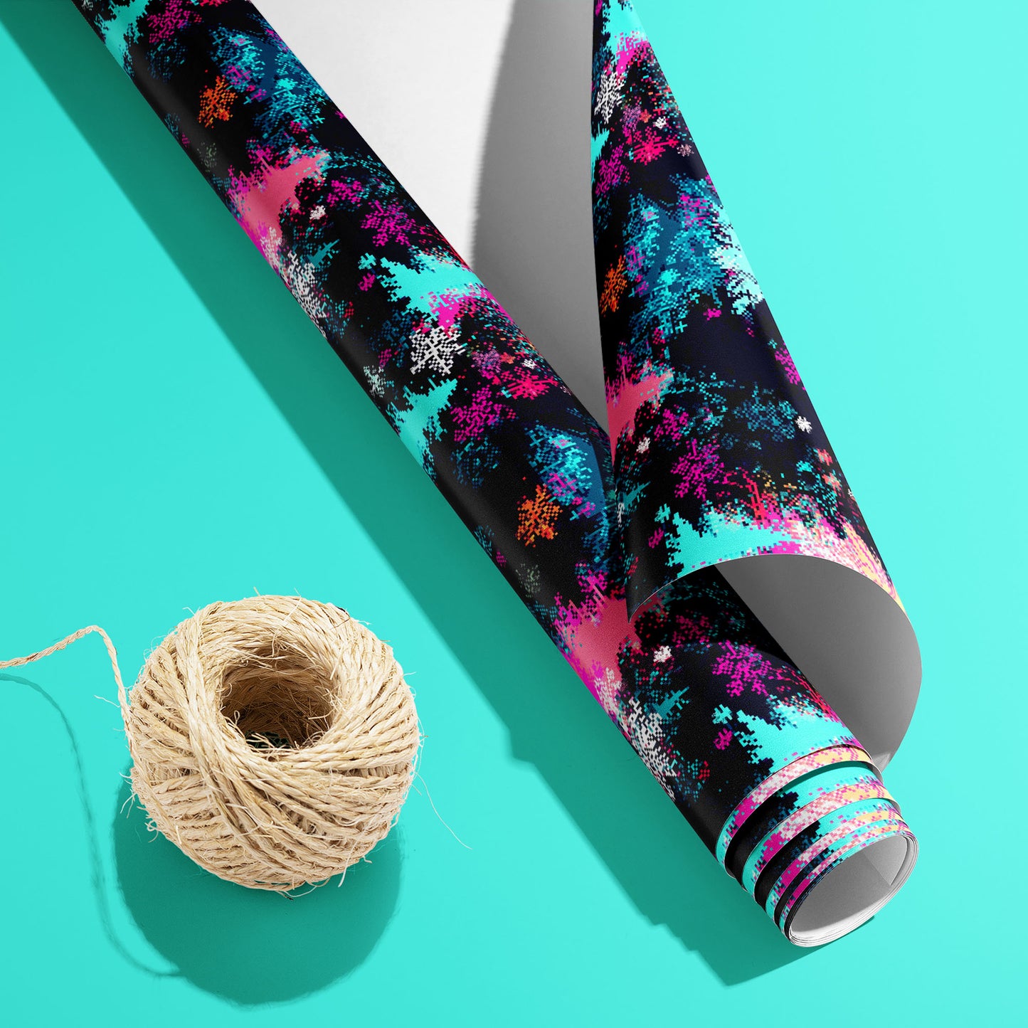 A partially unfurled roll of Pixel Pines with its white underside visible beside a spool of natural twine, showing pixelated trees and snowflakes on a soft teal surface.
