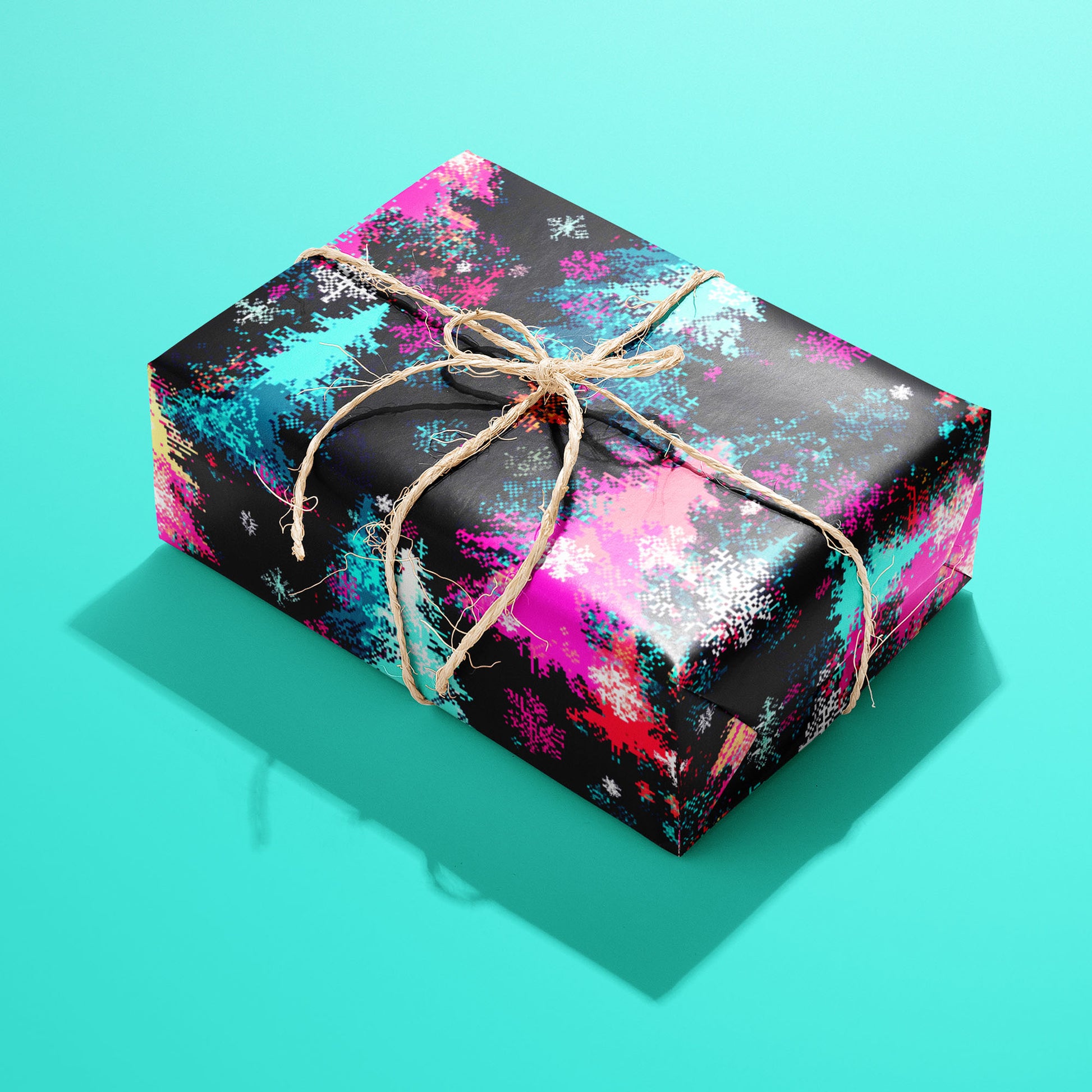A single gift wrapped in Pixel Pines and tied with natural twine, displaying retro 8-bit pine trees, ornaments, and snowflakes on a soft teal surface.
