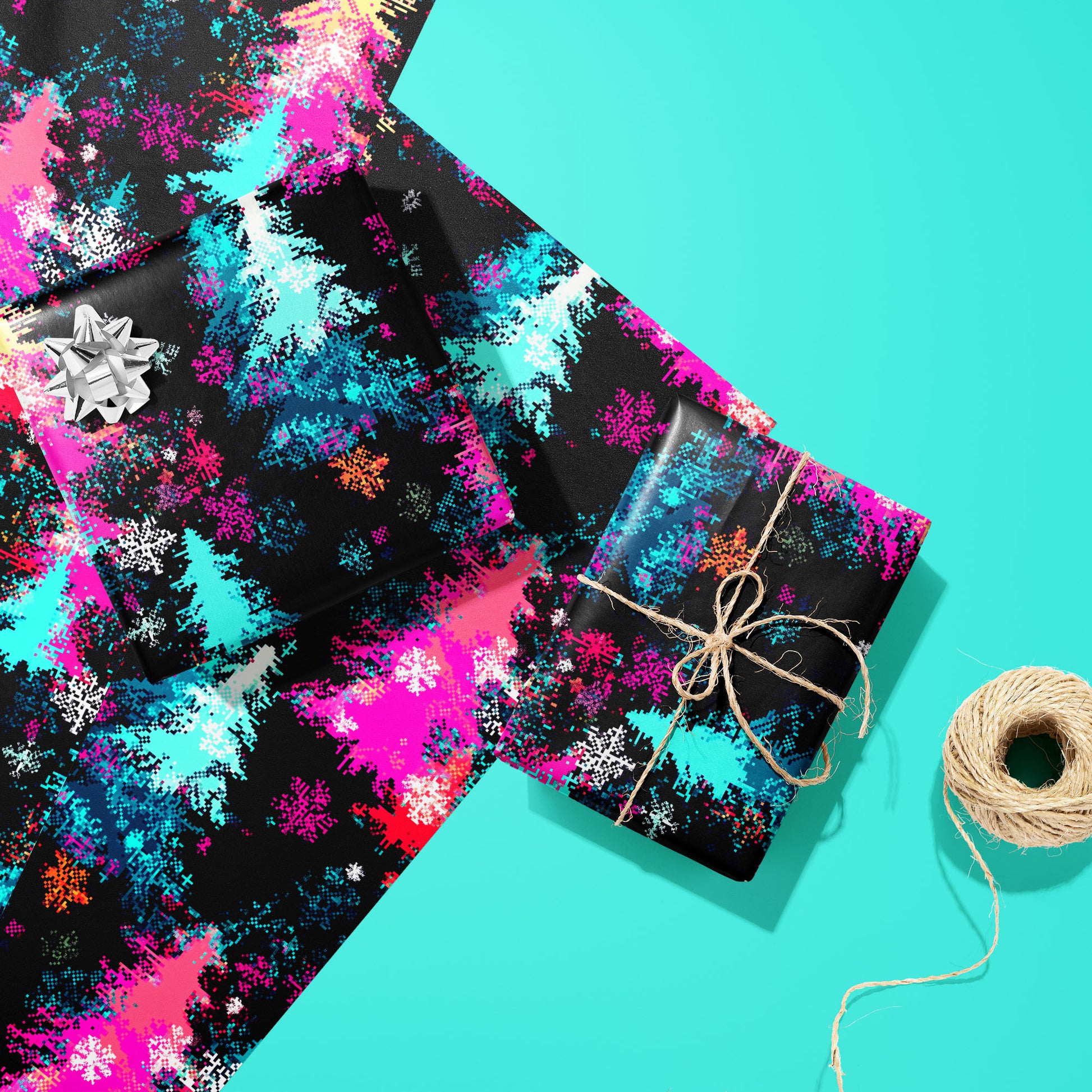 Two gifts wrapped in Pixel Pines—one with a silver bow and one tied with twine—rest on two unused sheets beside a twine spool on a soft teal surface with pixel-art pines and snowflakes.