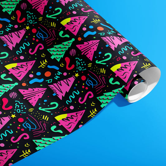 A partially unfurled roll of Electric Wonderland wrapping paper showing neon pink and green trees with Memphis squiggles and confetti on black, set against a bright blue surface.