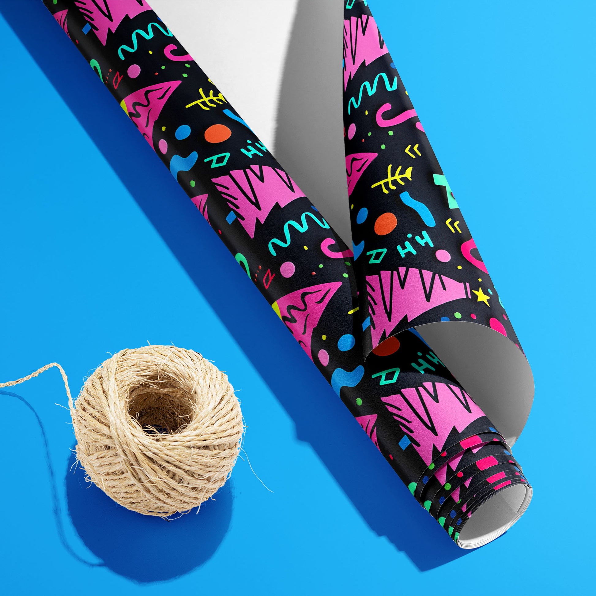 A partially unfurled roll of Electric Wonderland with the white underside visible beside a spool of natural twine on bright blue, featuring neon Memphis trees, squiggles, and dots on black.