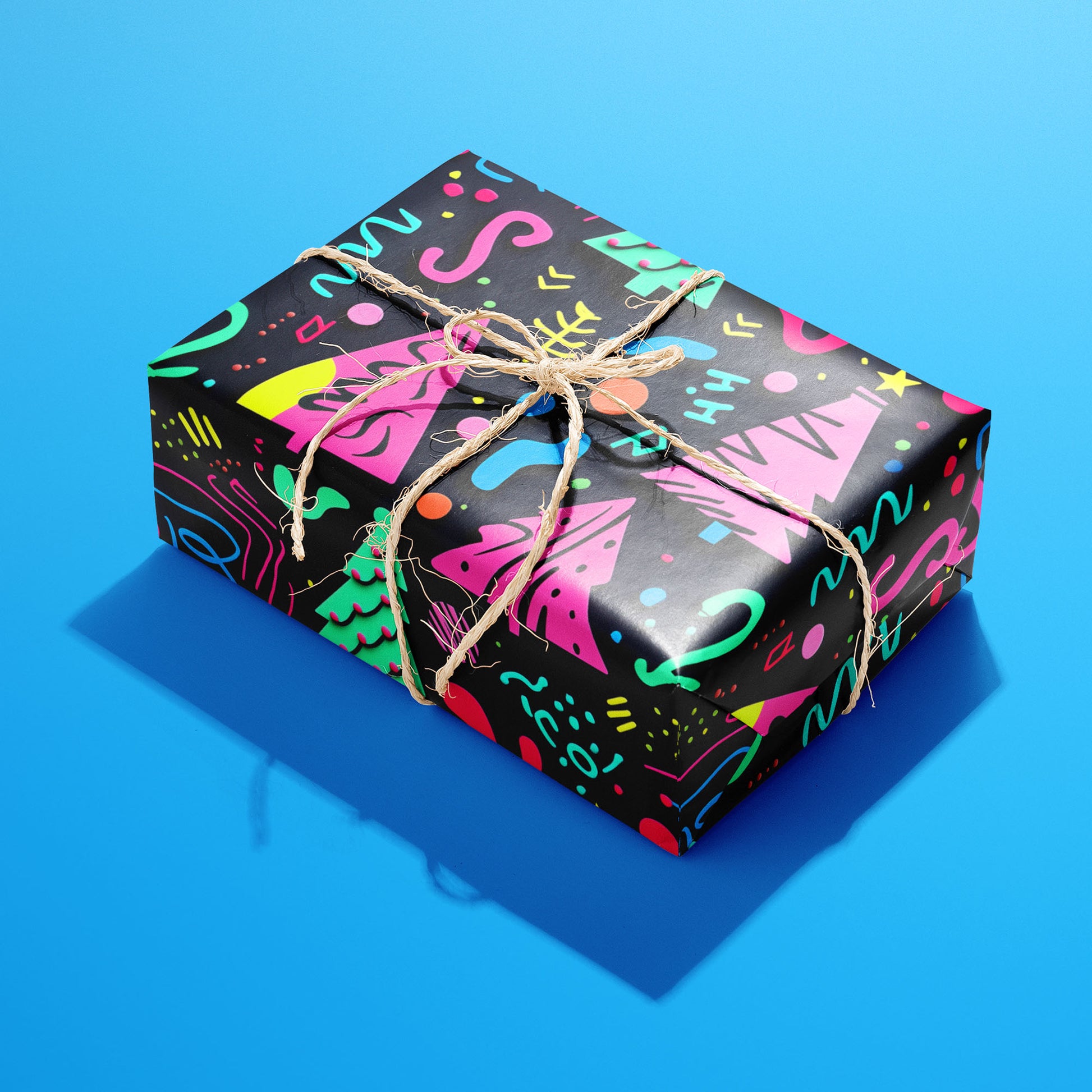 A single gift wrapped in Electric Wonderland and tied with natural twine, its neon Memphis trees and confetti on deep black popping against the bright blue background.