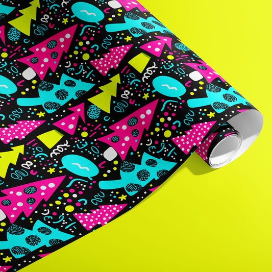 A partially unfurled roll of Neon Noel wrapping paper showing neon geometric trees and playful confetti marks on deep black against an acid-yellow background.