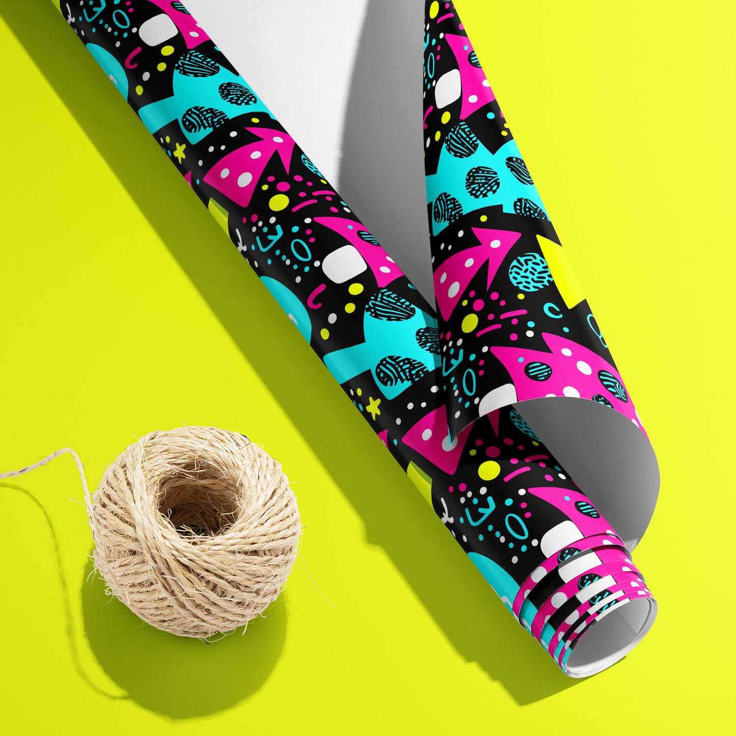 A partially unfurled Neon Noel roll with the white underside visible beside a spool of natural twine, featuring neon trees and abstract ornaments on an acid-yellow surface.