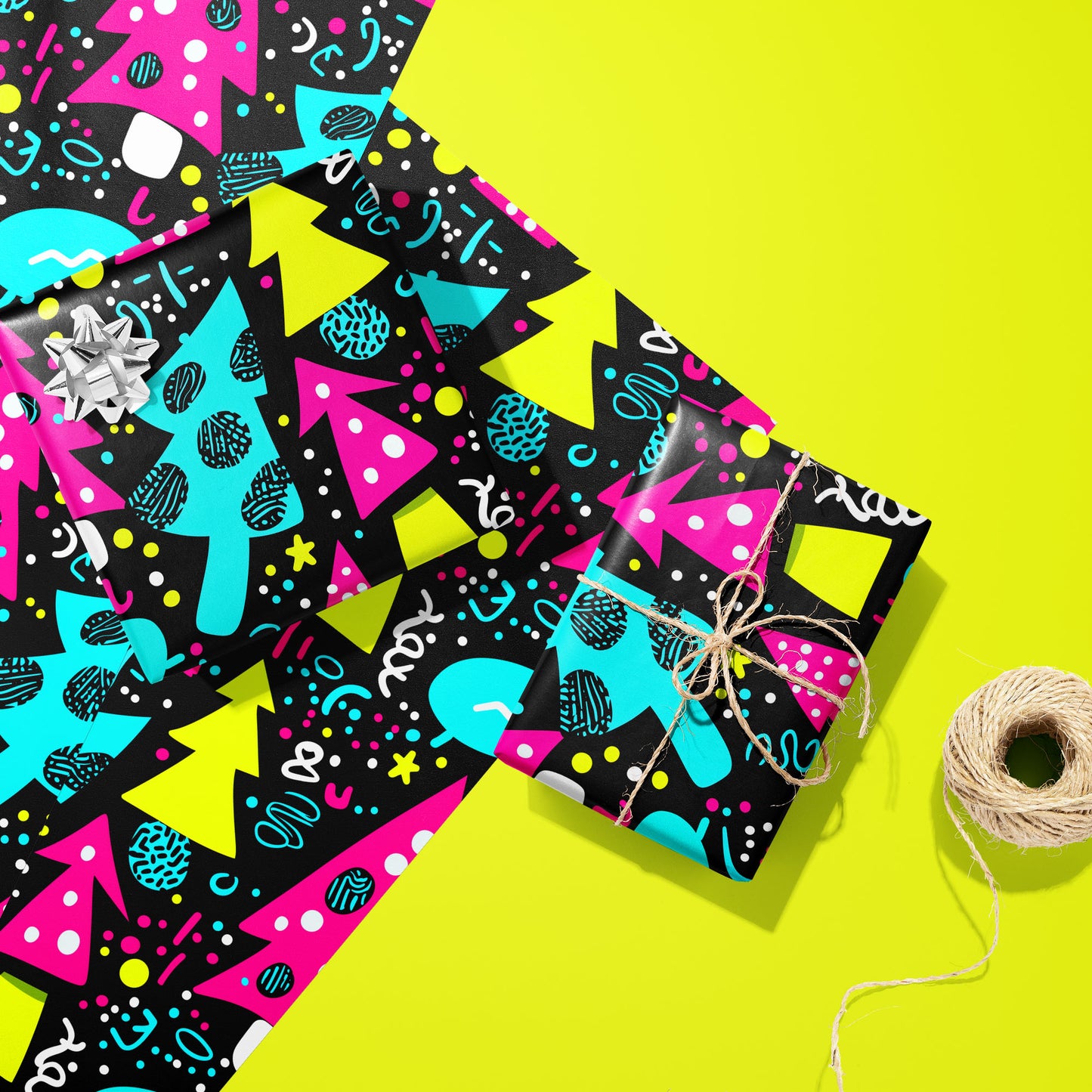 Two gifts in Neon Noel wrap—one with a silver bow and one tied with twine—rest on two unused sheets beside a spool of twine on an acid-yellow background.