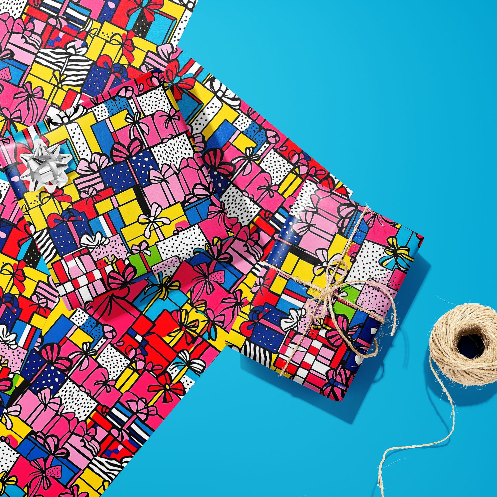 Two gifts in Pop Art Presents—one with a silver bow and one tied with twine—rest on two unused sheets beside a twine spool on a bright cyan surface, showing pop-art presents.