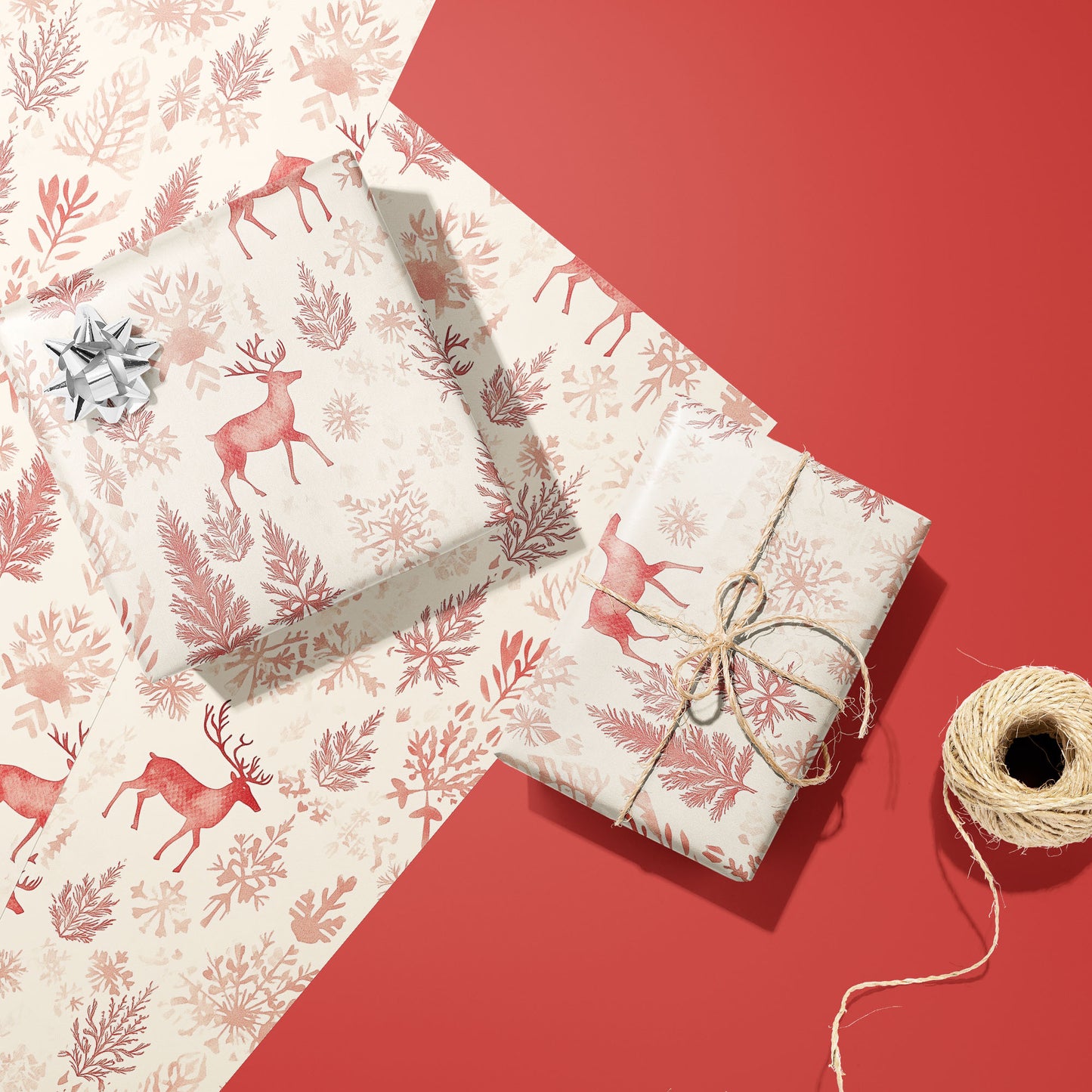 Two gifts wrapped in Nordic Wonderland reindeer-patterned paper, one with a silver bow and one tied with twine, rest on extra sheets beside twine on a red surface.