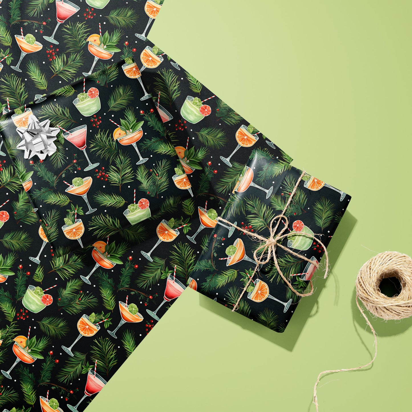Two gifts wrapped in Holiday Cocktails cocktail-patterned paper, one with a silver bow and one tied with twine, resting on extra sheets beside a spool of twine.