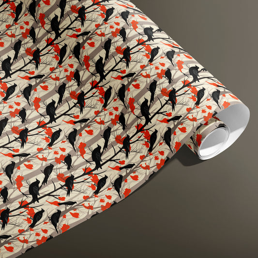 A partially unfurled roll of Raven's Reverie wrapping paper showing silhouetted ravens, branches, and red leaves across taupe tree trunks on a smoky taupe background.