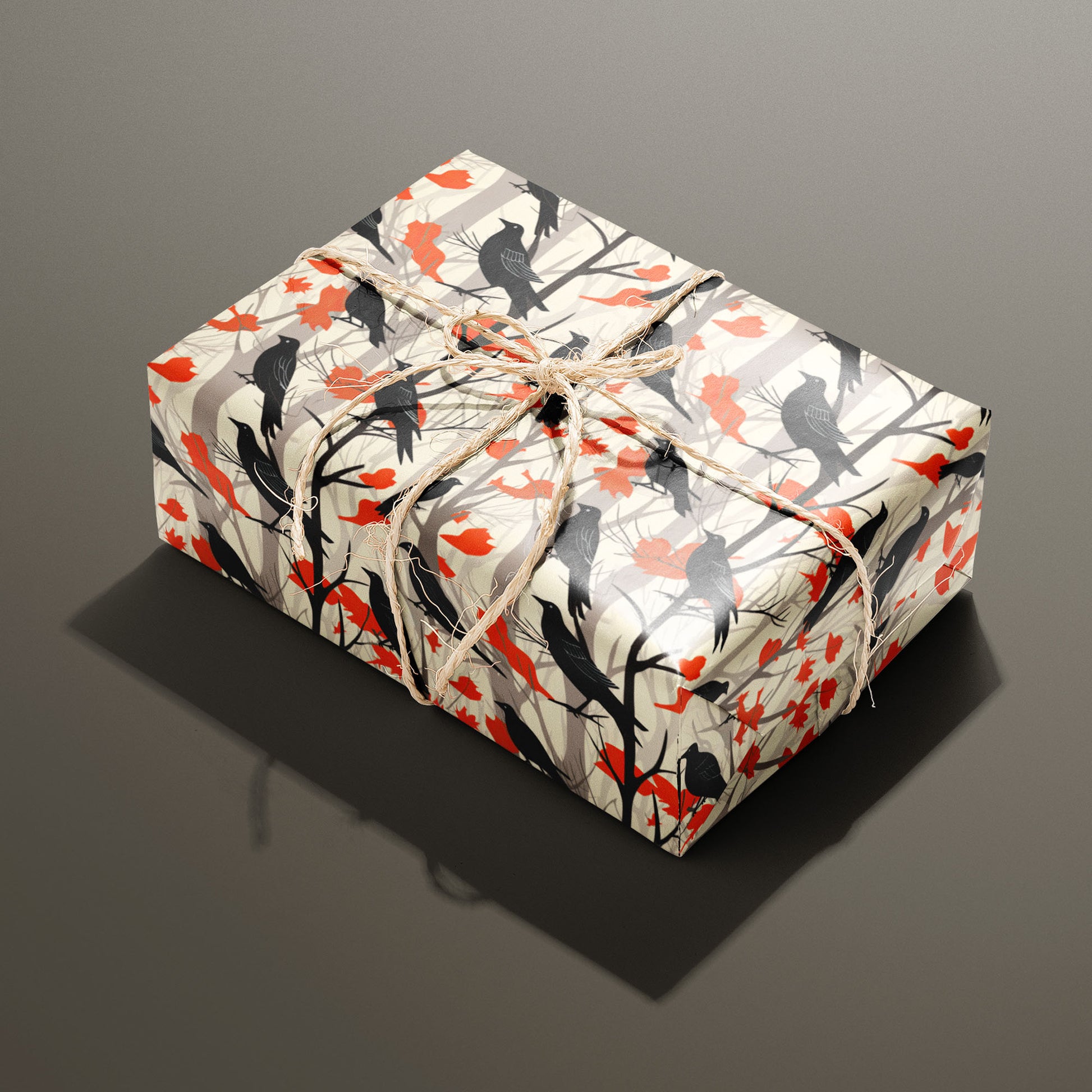 A single rectangular gift wrapped in Raven's Reverie—black ravens, branches, and scarlet leaves—tied with natural twine on a smoky taupe background.