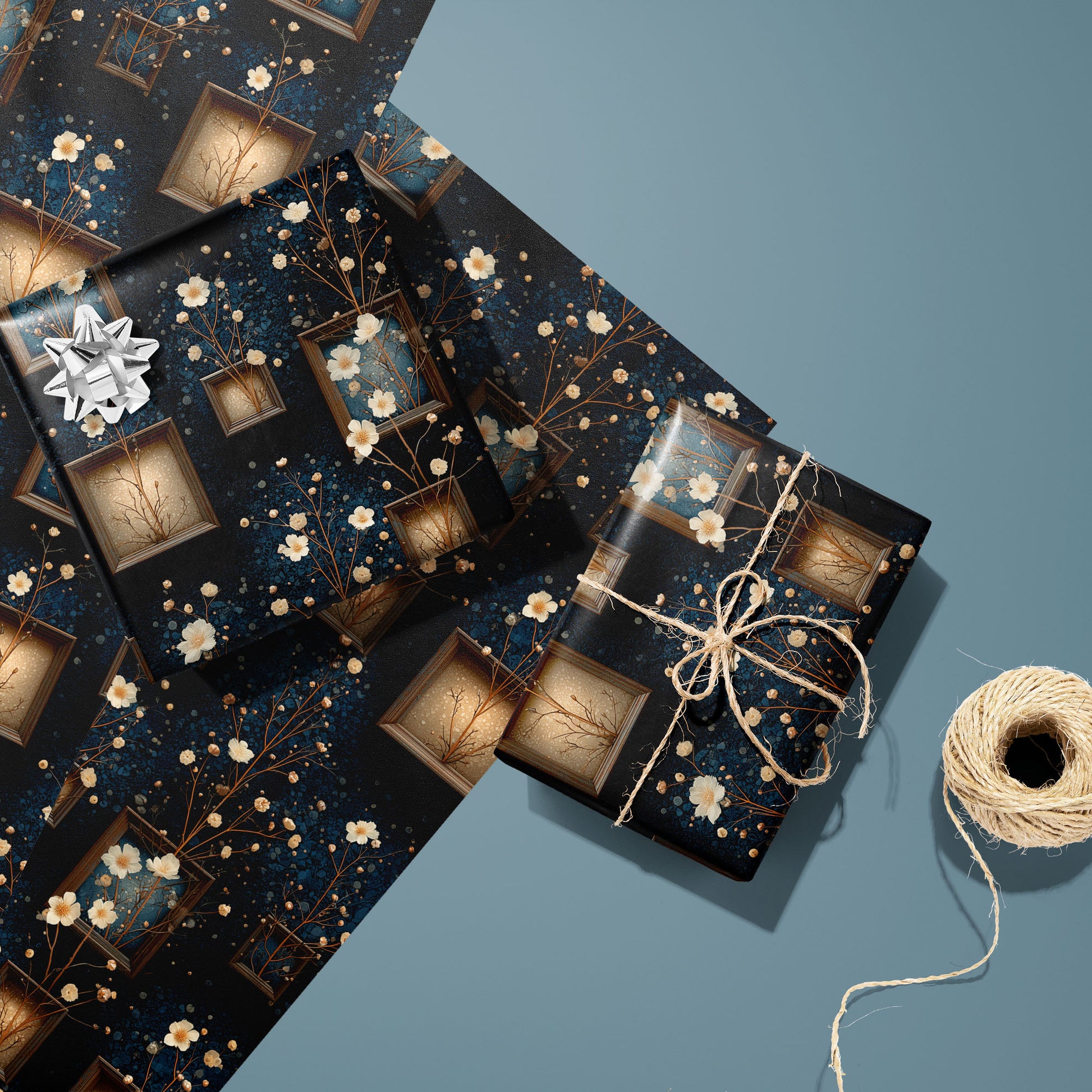 Two gifts wrapped in Curio Florarium—one topped with a silver bow and one tied in natural twine—rest on two unused sheets, showing vintage frames and cream blossoms on deep navy against a teal background.