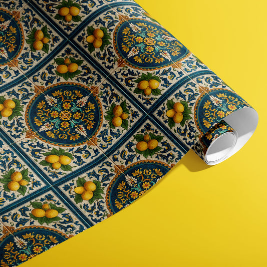 A partially unfurled roll of Citron Azulejo wrapping paper showcasing blue ceramic tile motifs with lemons and filigree florals against a vivid yellow surface.