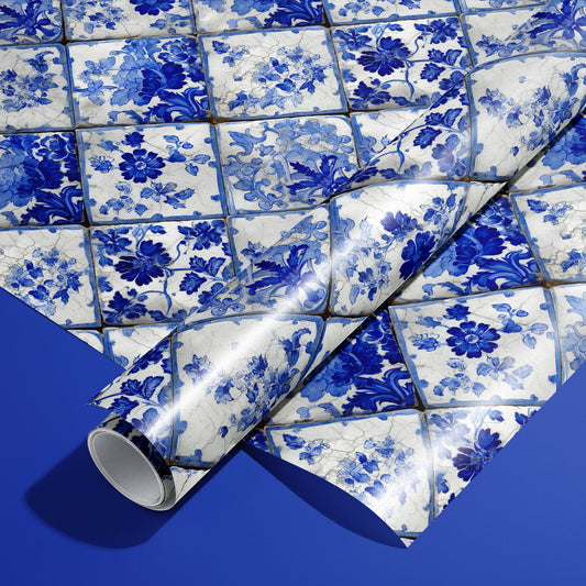 A roll of Aegean Bouquet wrapping paper resting on a full sheet, showing blue-and-white floral azulejo tiles with crackle details on a rich royal blue background.