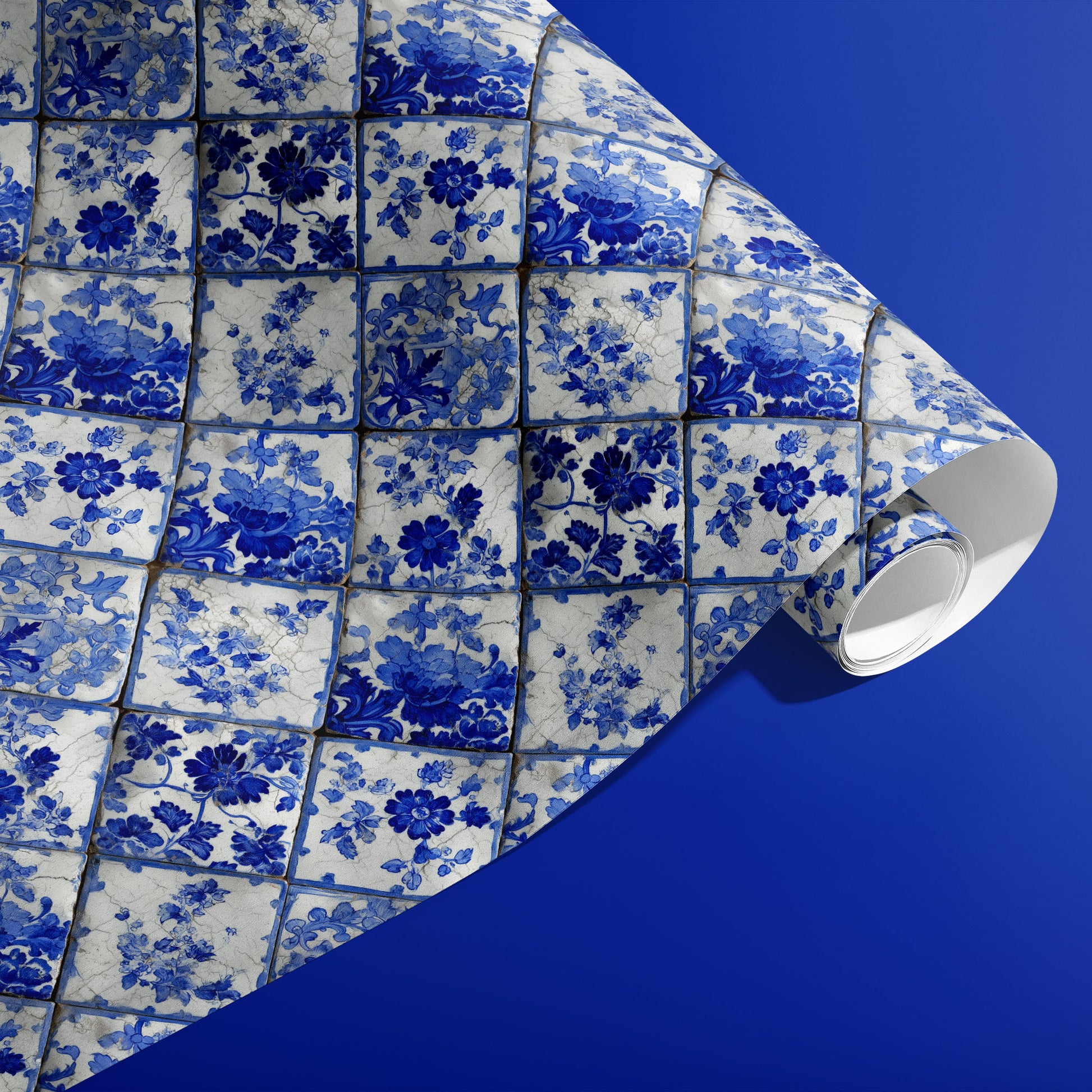 A partially unfurled roll of Aegean Bouquet wrapping paper featuring Delft-style floral tiles in cobalt and ivory against a deep blue surface.
