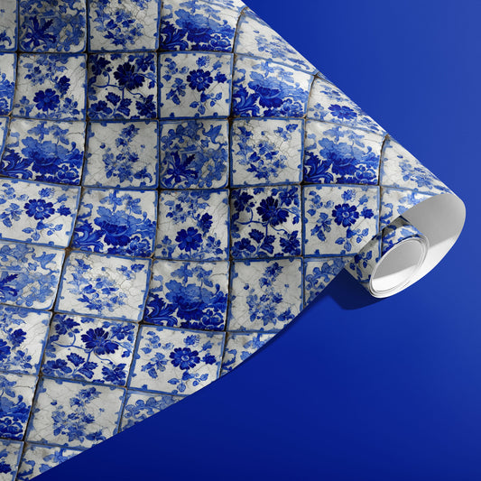 A partially unfurled roll of Aegean Bouquet wrapping paper featuring Delft-style floral tiles in cobalt and ivory against a deep blue surface.