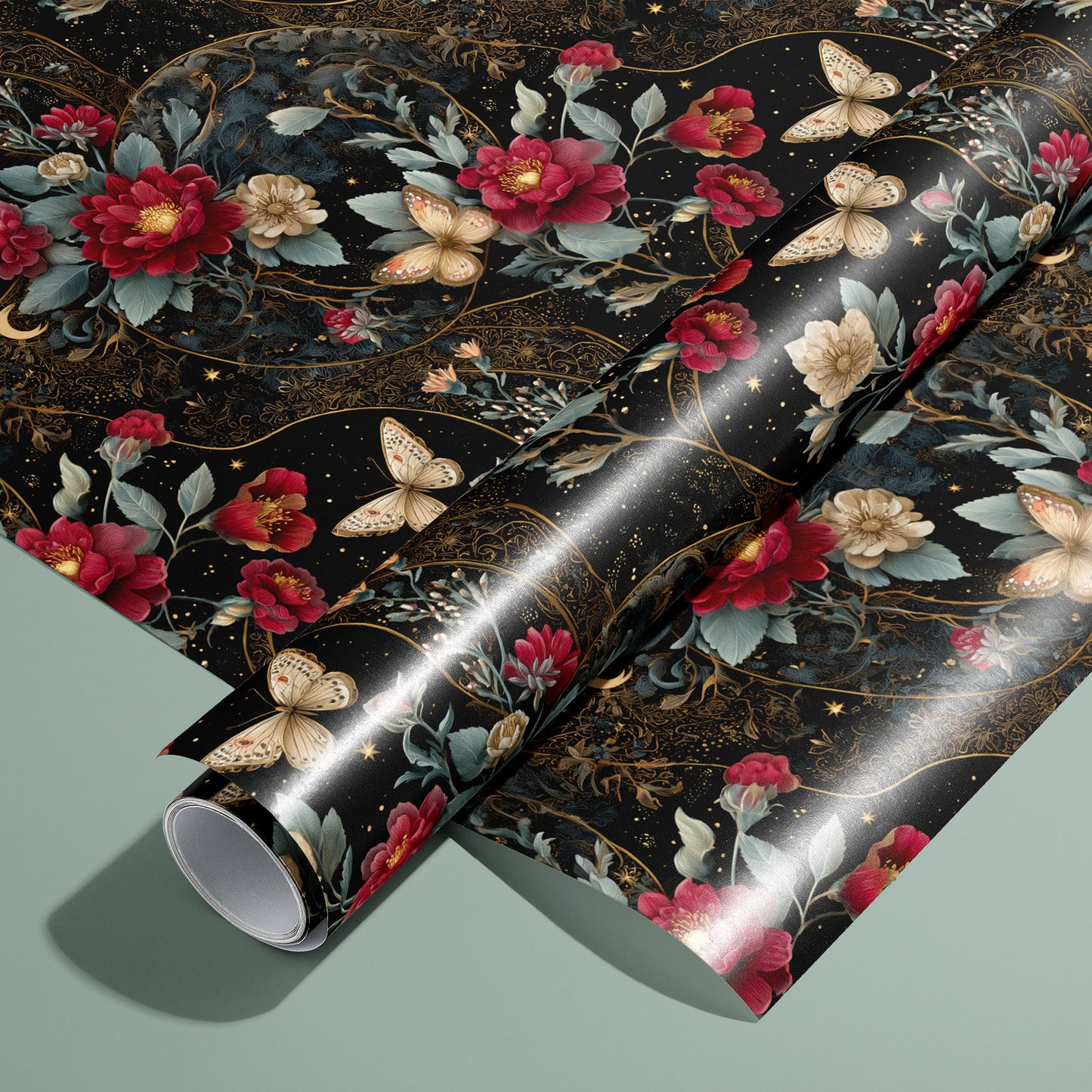 A roll resting on an unrolled sheet of Velvet Asterism wrapping paper, a black celestial floral with red and cream blooms, butterflies, and gold filigree, on a sage green surface.