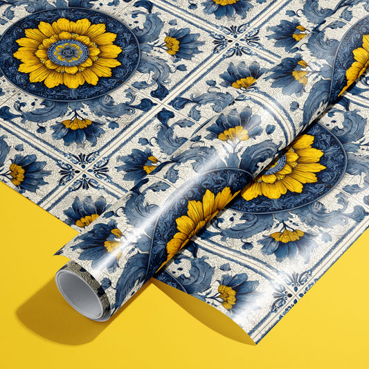 A roll of Lapis Florale wrapping paper resting on a full sheet, showcasing blue-and-gold sunflower medallions and baroque azulejo scrolls on a sunny yellow background.