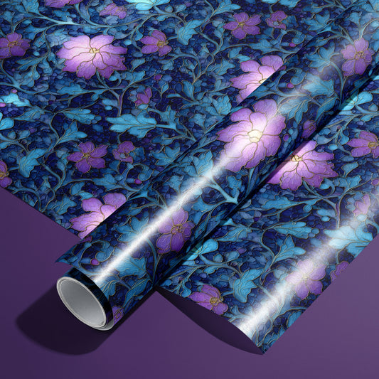 A roll of Lunar Hellebore wrapping paper on an unrolled sheet, showing violet hellebore blooms with teal foliage on midnight blue, set on a deep purple surface.