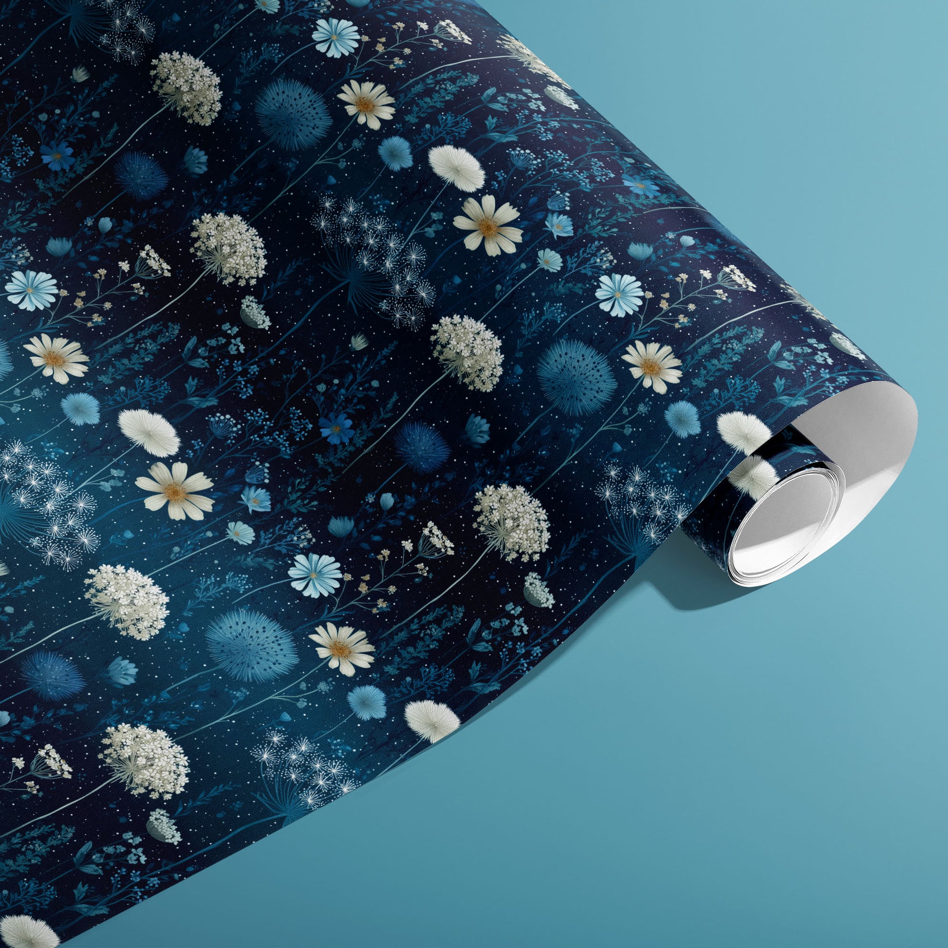 A partially unfurled roll of Midnight Garden wrapping paper showing blue botanical blooms and tiny starry dots on a deep navy ground, on a teal background.